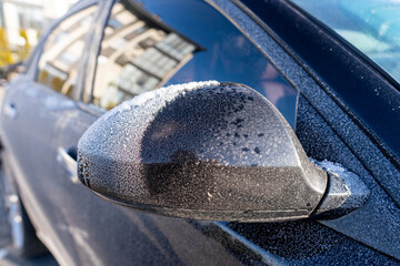 A car's side mirror is covered in ice. The mirror is black and has a frosty appearance