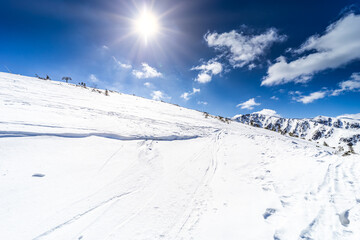 A bright winter sun with a starburst effect shining over a pristine, snow-covered mountain ridge under a clear blue sky in the Low Tatras, Slovakia.