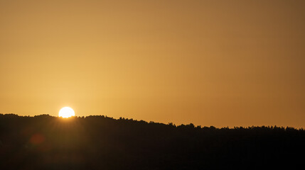 Golden hour over a quiet lake with the sun shining on reflective water and silhouetted hills on the horizon. Evocative sunset landscape with warm light and calm mood, suited for backgrounds.