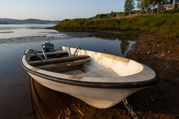 A white fishing boat tied to the shore provides a focal point in the foreground, while warm morning light illuminates the water's surface.