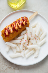 White plate with korean tteokbokki or garaetteok and a corn-dog, vertical shot, middle close-up, elevated view