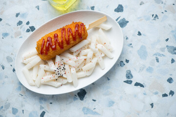 Korean traditional tteokbokki or rice cakes with a corn-dog, horizontal shot on a white and blue granite background with space, top view