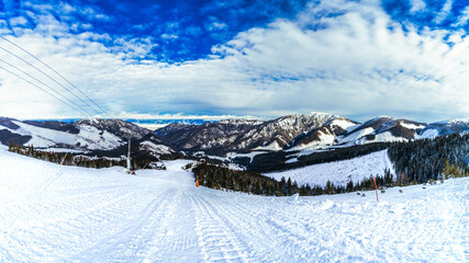 A scenic wide-angle panorama of a groomed ski slope in the Low Tatras, Slovakia, featuring ski lift...