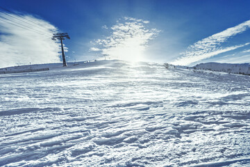 A wide scenic shot of a groomed ski slope in the Low Tatras, Slovakia, under a dramatic cloudy sky during twilight, featuring snow-covered ridges and evergreen forests.