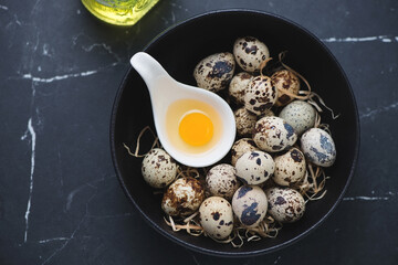 Bowl with raw fresh quail eggs on a black marble background, horizontal shot, above view