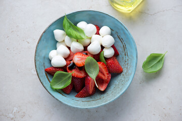 Caprese with fresh strawberry, mini mozzarella cheese and fresh basil in a turquoise bowl, horizontal shot on a light-beige stone background