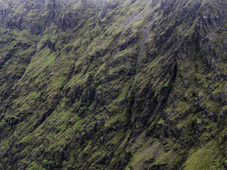 A steep mountainside features green moss growing on rocks. Grey cliffs and ravines cut through the terrain.