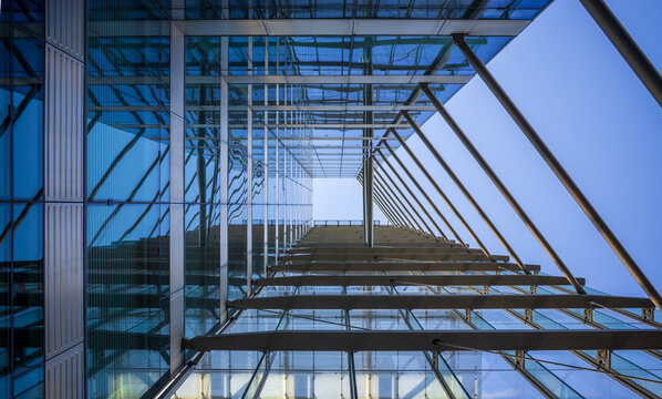 Abstract upward view of a modern glass and steel building facade with strong reflections and geometric architectural lines against a clear blue sky