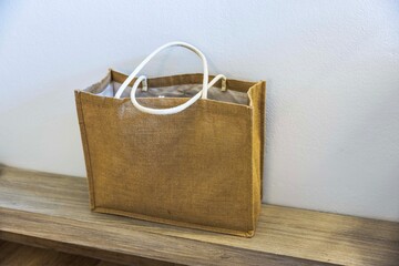 Close up view of brown beach bag with handles standing on wooden surface against light wall. Greece.