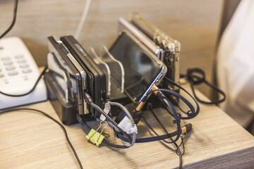 Close up view of charging station with multiple smartphones and cables on hotel bedside table. Greece.
