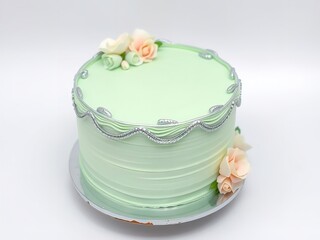 A beautifully decorated mint green cake with flowers and silver trim on a white background