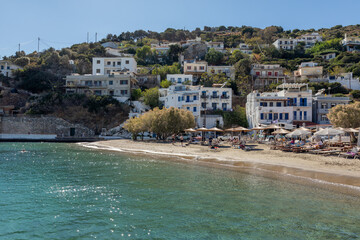 Fototapeta premium Turquoise water and sandy beach in the seaside village of Therma on Ikaria island, Greece. Traditional houses along the coast, summer atmosphere and Mediterranean travel destination.