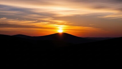 Radiant sun peeking over a distant mountain range creating a beautiful silhouette against a