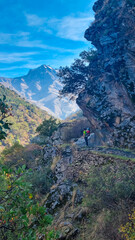 A hiker carrying a child stands on a cliffside path beneath a lone tree, gazing at the majestic La Alcazaba peak on the Vereda de la Estrella trail in Sierra Nevada, Granada, Andalusia, Spain.