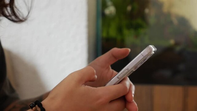 A close detailed view of a woman hands holding a smartphone in a cafe, fingers interacting with the screen, the frame focusing on touch, attention, and everyday digital interaction. Mobile lifestyle.