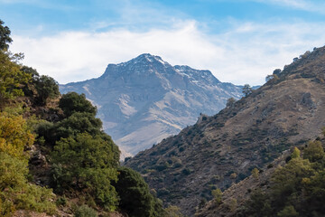 Impressive north face of the Mulhacen and Alcazaba mountains towers over the deep rugged Genil valley, seen from the Vereda de la Estrella trail in Sierra Nevada National Park, Andalusia, Spain.