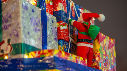 Small Santa Claus figure attached to colorful gift boxes with festive lights