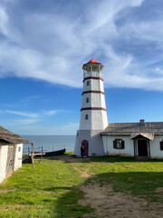 A beautiful lighthouse overlooks the calm sea on a sunny day with historic buildings nearby