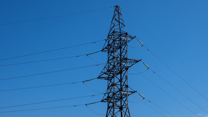 High-voltage tower with power line wires on background clear blue sky. Summer sunny day