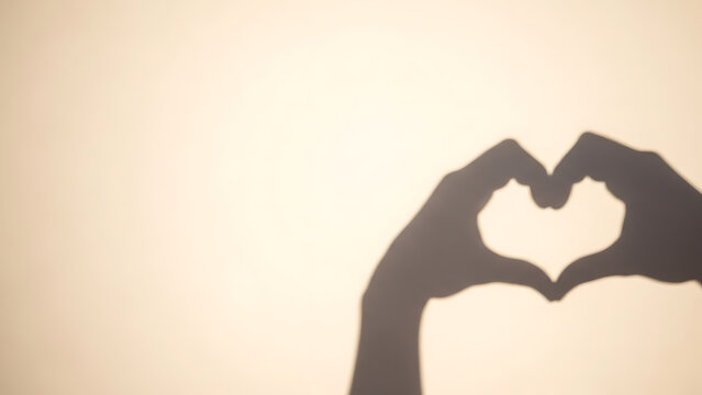 Shadow of hands forming a heart shape on a warm-toned background, symbolizing love and affection.