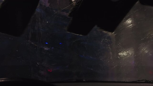 Car wash scene, Motion and light interplay during automatic car wash at nighttime with sudsy glass