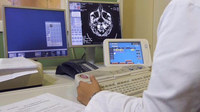 A radiology technician works on a computer with CT scans of the skull, close up