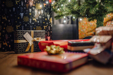 Festively wrapped presents in various colors and patterns are arranged under a Christmas tree, creating a warm and inviting holiday atmosphere with twinkling lights