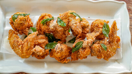 Golden crispy fried chicken pieces garnished with curry leaves served on white ceramic plate. Asian spicy comfort food with crunchy texture, ideal for restaurant menus and food advertising