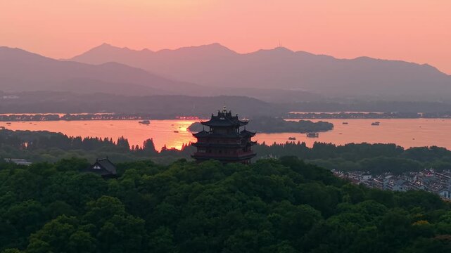 Aerial view of Chenghuang pagoda at sunset over Xihu lake in Hangzhou featuring mountains and lush green trees