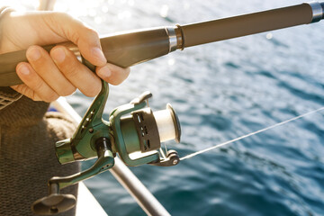 Close up of hands holding a fishing rod with a spinning reel over a sea background.