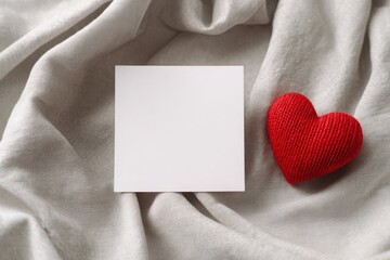 A red heart rests on a silver fabric backdrop, with a blank space for a message, perfect for Valentines Day.