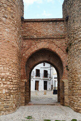 Historic Puerta de Almoc&aacute;bar in Ronda, a fortified medieval gate with stone walls and brick horseshoe arch, opening toward the old town and highlighting the city&rsquo;s Andalusian architectural heritage.