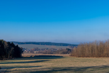 Expansive blue sky over a serene landscape with rolling hills and distant village nestled in nature's tranquility