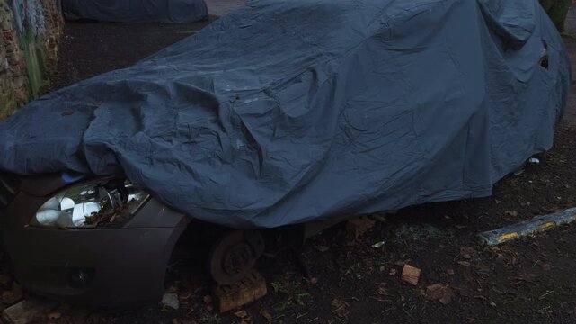 Vehicle with missing wheel by graffiti wall, Neglected hatchback resting beside graffiticovered wall