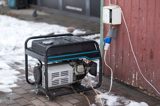 Portable gasoline generator connected to outdoor power socket near building during winter, emergency electricity supply concept.