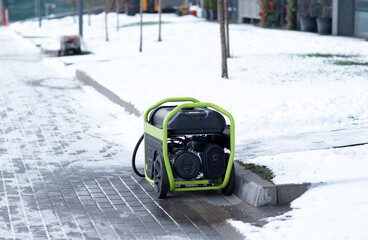 Portable electric generator standing on a snowy sidewalk near a curb in winter urban environment, outdoor power equipment concept.