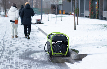 Portable lime green gas generator operating on a snowy sidewalk as people walk past in a winter city.