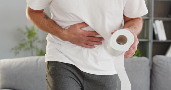 Man diarrhea stomachache bloating pain cramp toilet paper urgency. Adult male clutching abdomen at home, suffering digestive distress, gas and nausea. Strong concept of digestive urgency.