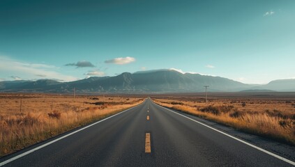 An empty roadway surrounded by mountains beneath a bright, cloudless sky, highlighting remote transportation routes