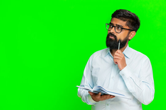 Indian man writes in notebook with serious focused expression, planning daily tasks and organizing to-do list. Arabian guy isolated on green chroma key background showing concentration and preparation - Powered by Adobe