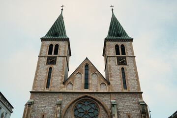 Fototapeta premium Front view of historic cathedral facade with twin towers in morning Sarajevo. Architectural symmetry and soft sky emphasize cultural identity and timeless religious heritage.