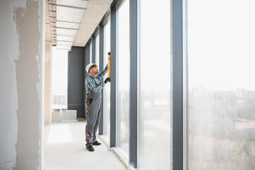 Construction worker using spirit level on window frame in building under construction