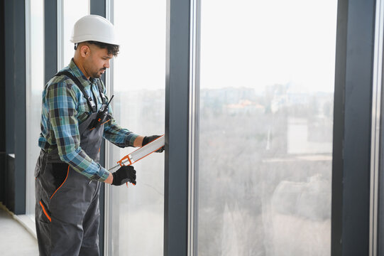 Construction worker sealing window frame in modern building