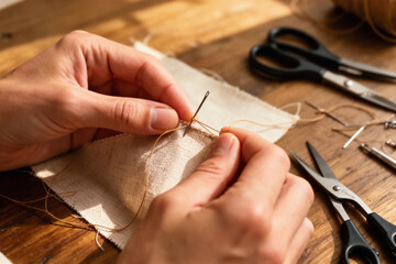 Hands sewing fabric on wooden craft table.