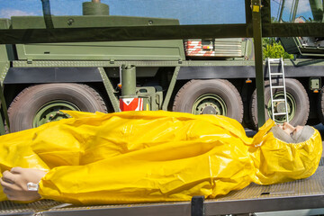 Rescue drill with mannequin in protective clothing, medical equipment, tent structure and large german military vehicle in background. Simulation of decontamination and medical care