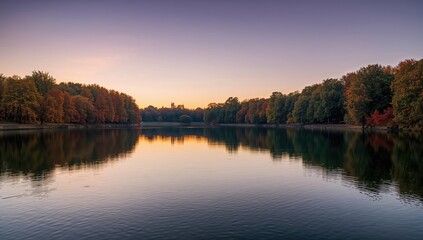 Obraz premium Reflective lake surface captures colorful fall leaves and trees at dusk in an urban park setting