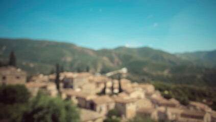 Obraz premium Out-of-focus view of a Mediterranean village with stone cottages and lush hills beneath a clear blue sky, ideal for travel content