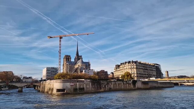 A scenic view of the Notre-Dame Cathedral in Paris from the Seine River. The historic Gothic structure is undergoing restoration with a large crane visible. Classic Parisian cityscape atmosphere