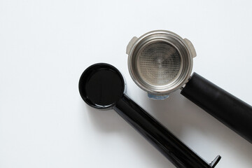 A metal coffee portafilter and measuring spoon on a white background