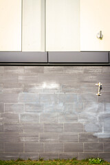 Dirty gray tile wall with some green grass underneath on a sunny day. Architectural detail.